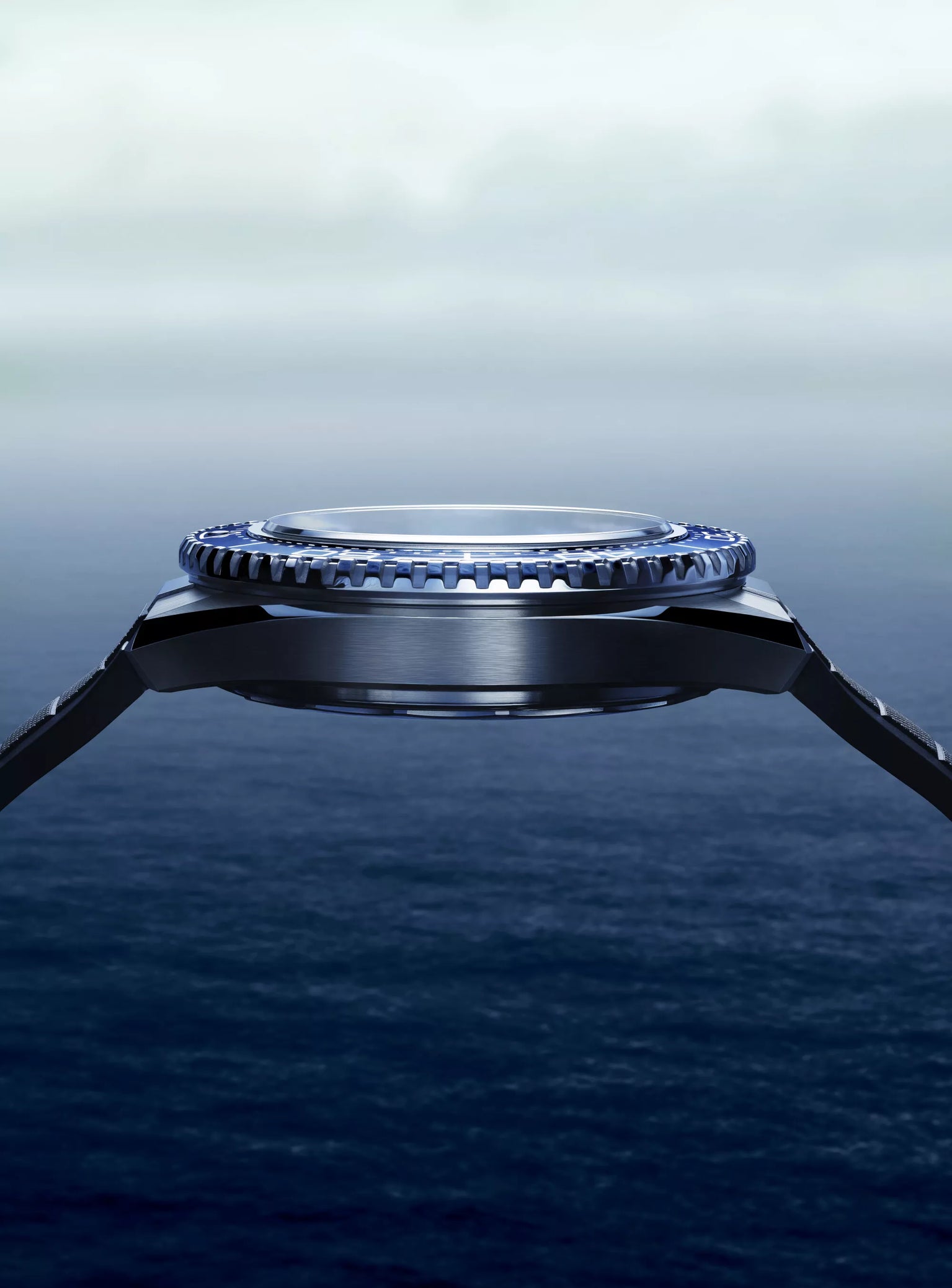 A close-up side view of the OMEGA Seamaster Planet Ocean 600mm dive watch with a blue bezel, set above a tranquil blue ocean beneath a hazy, cloud-filled sky.