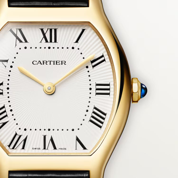 Gold-tone Cartier watch with white dial, Roman numerals, and blue crown, shown at angle with black leather strap.