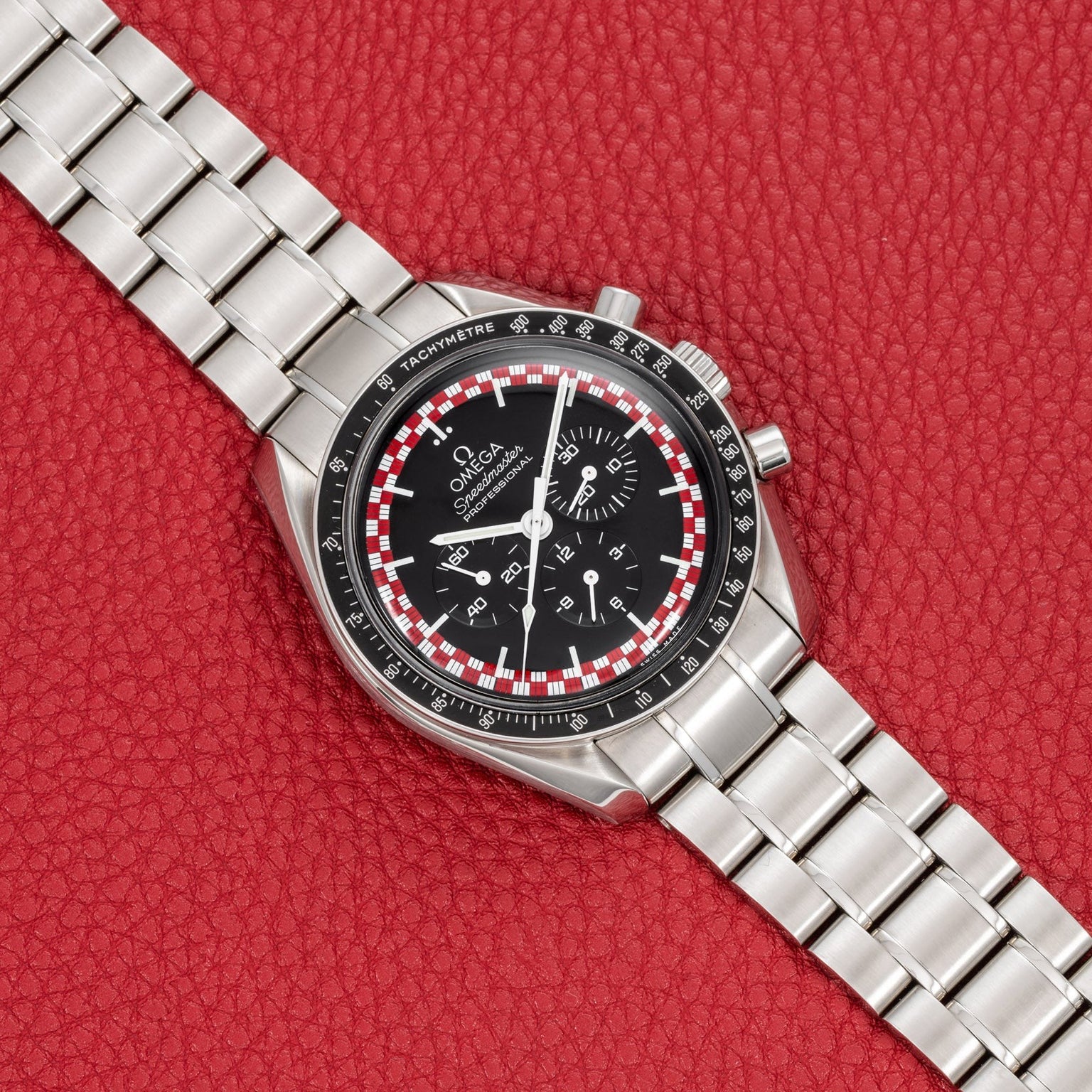 An OMEGA Speedmaster Tintin watch with a black dial and silver case displayed on a red textured background.