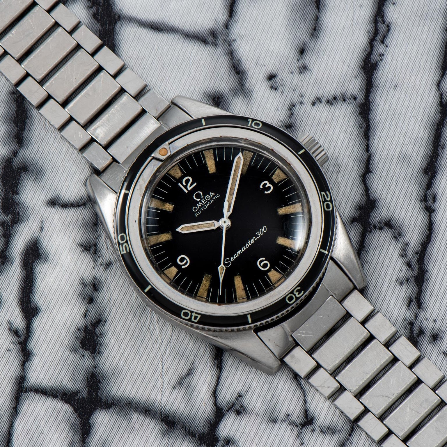 An OMEGA Seamaster 300 watch with a metal band displayed on a marble-patterned surface.