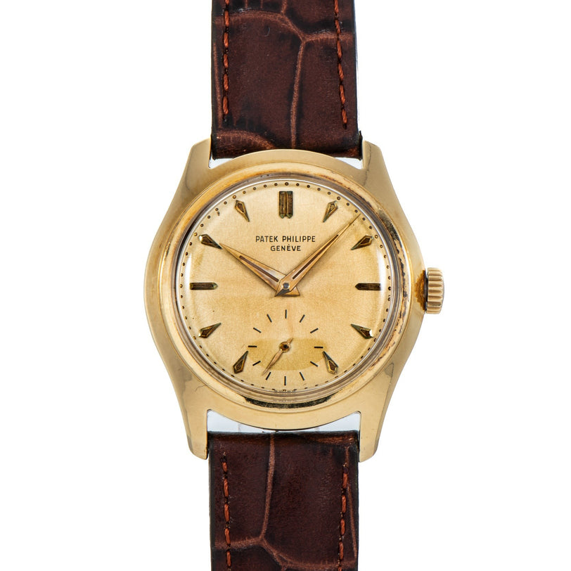 A Patek Philippe Calatrava vintage gold wristwatch featuring a round cream dial and brown leather strap.