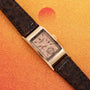 The Patek Philippe Tegolino Dress Watch, featuring a rectangular gold case and dark leather strap, is displayed on an orange textured background.