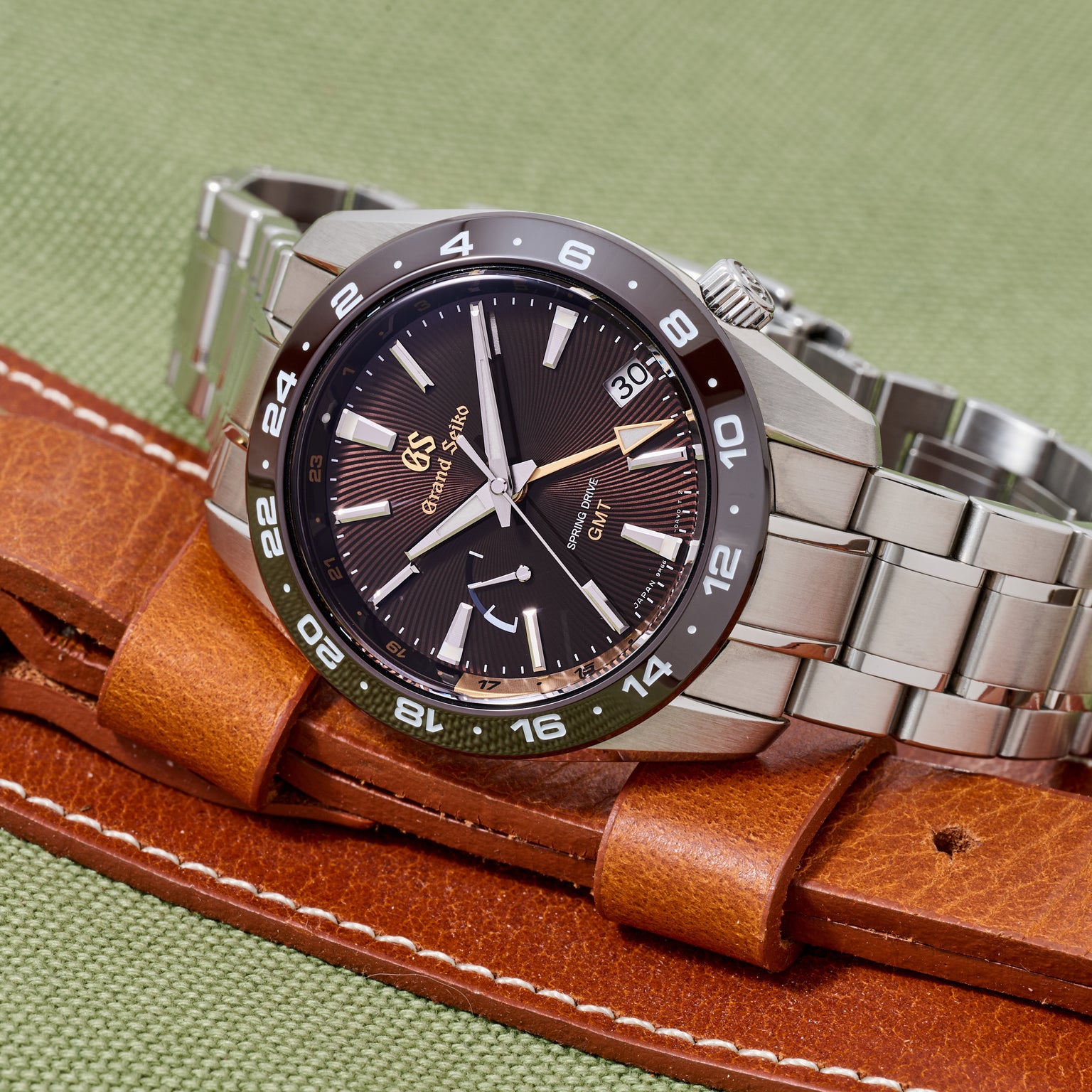 Watch with brown leather strap and silver metal case on green background