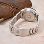 Silver watch with a detailed back cover on a beige surface