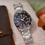 Silver wristwatch with a black dial on a textured surface with leather cases.