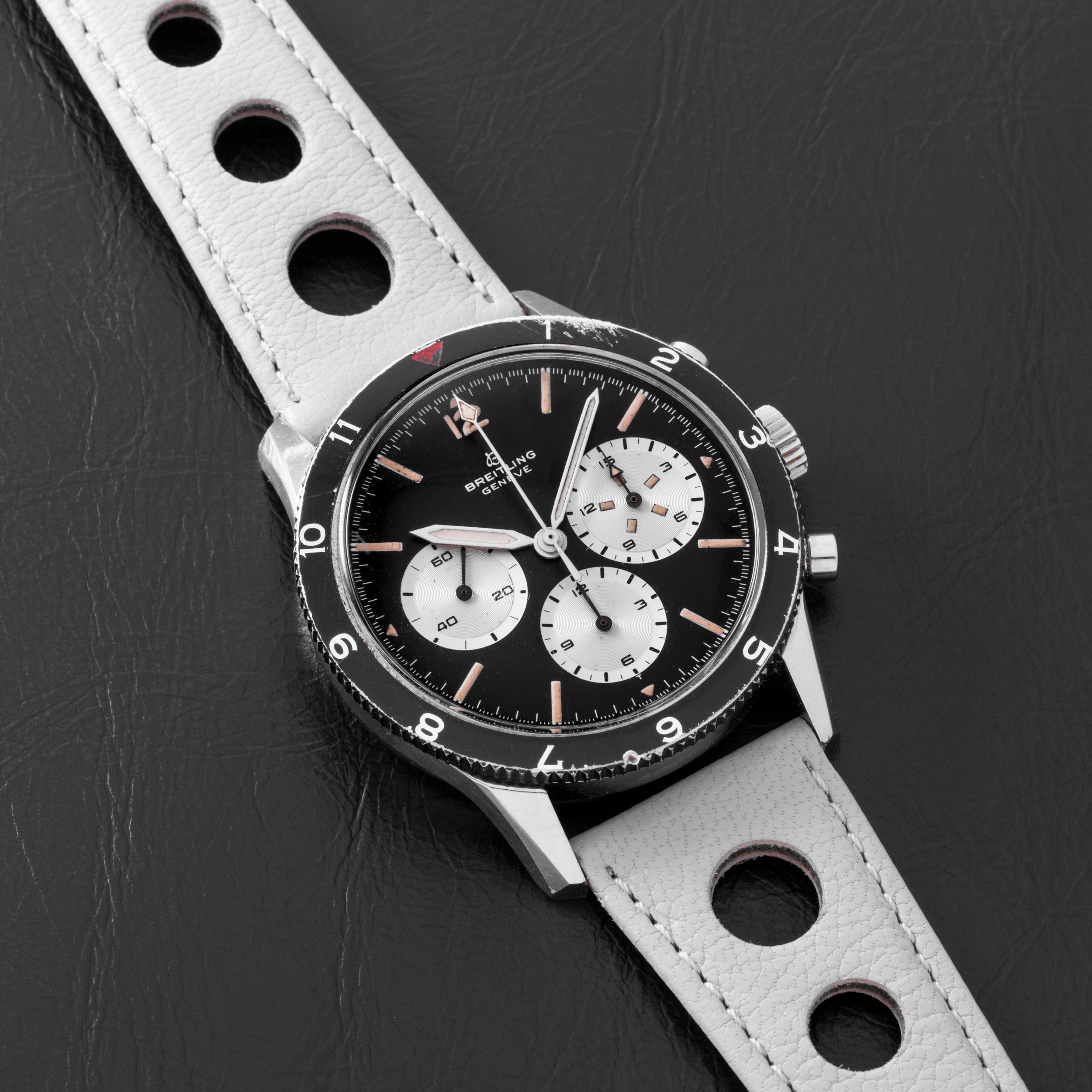 The Breitling Co-Pilot Chronograph, featuring a black and white dial and a perforated white leather strap, is displayed on a black surface.