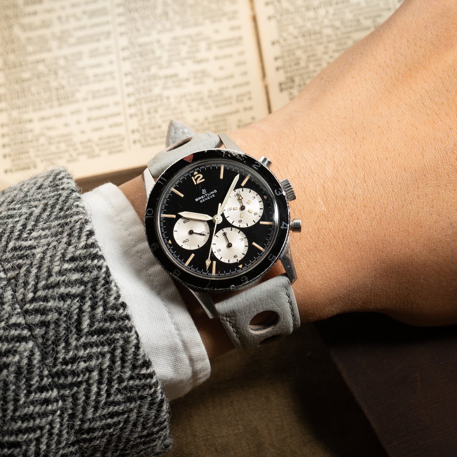 A wrist wearing the Breitling Co-Pilot Chronograph, paired with a herringbone jacket, rests beside an open book.