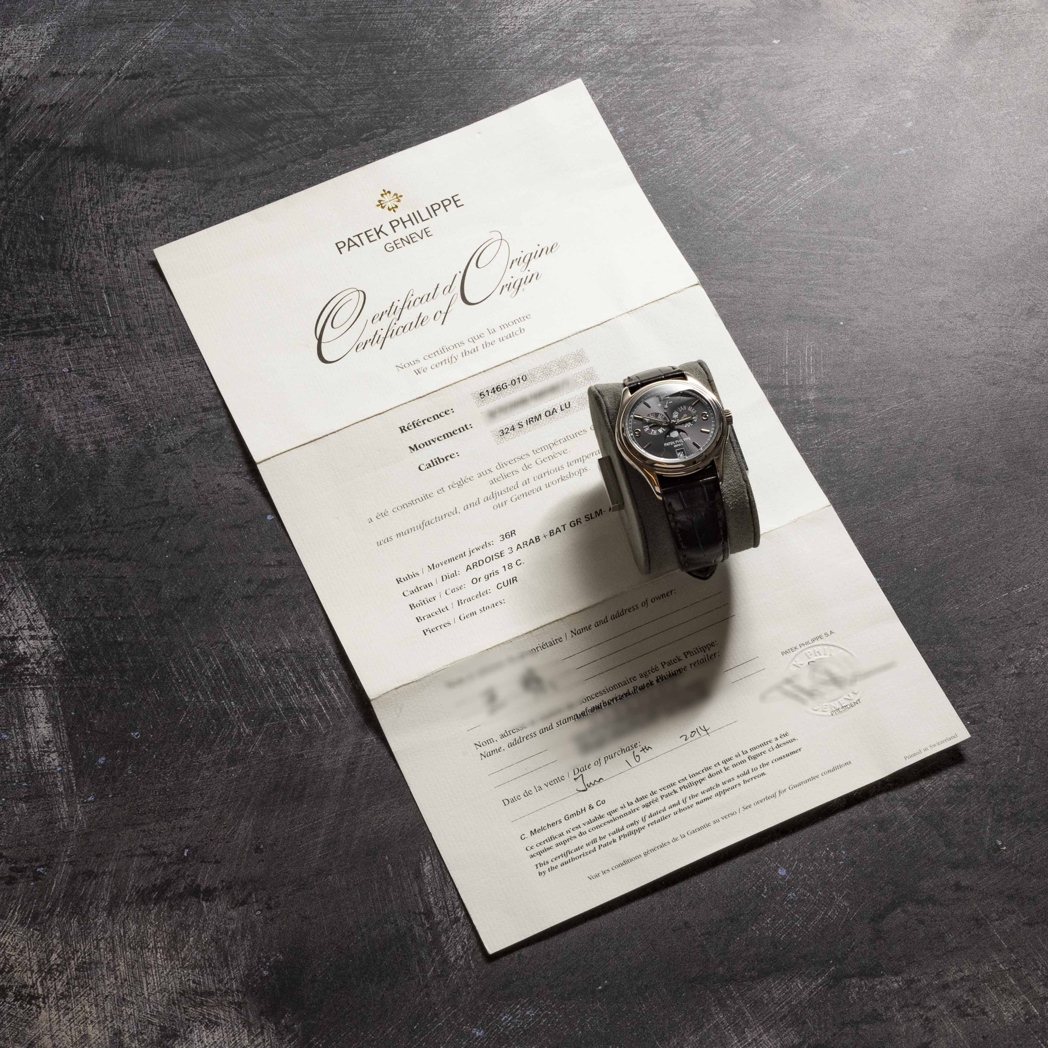 The Patek Philippe Annual Calendar Moonphase watch rests on a Certificate of Origin atop a dark, textured surface.