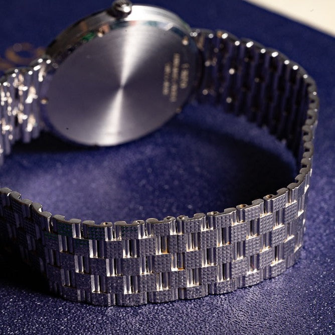 Close-up of the Audemars Piguet Classic White Gold Ultra-Thin watch with a textured bracelet, resting on a dark blue surface.