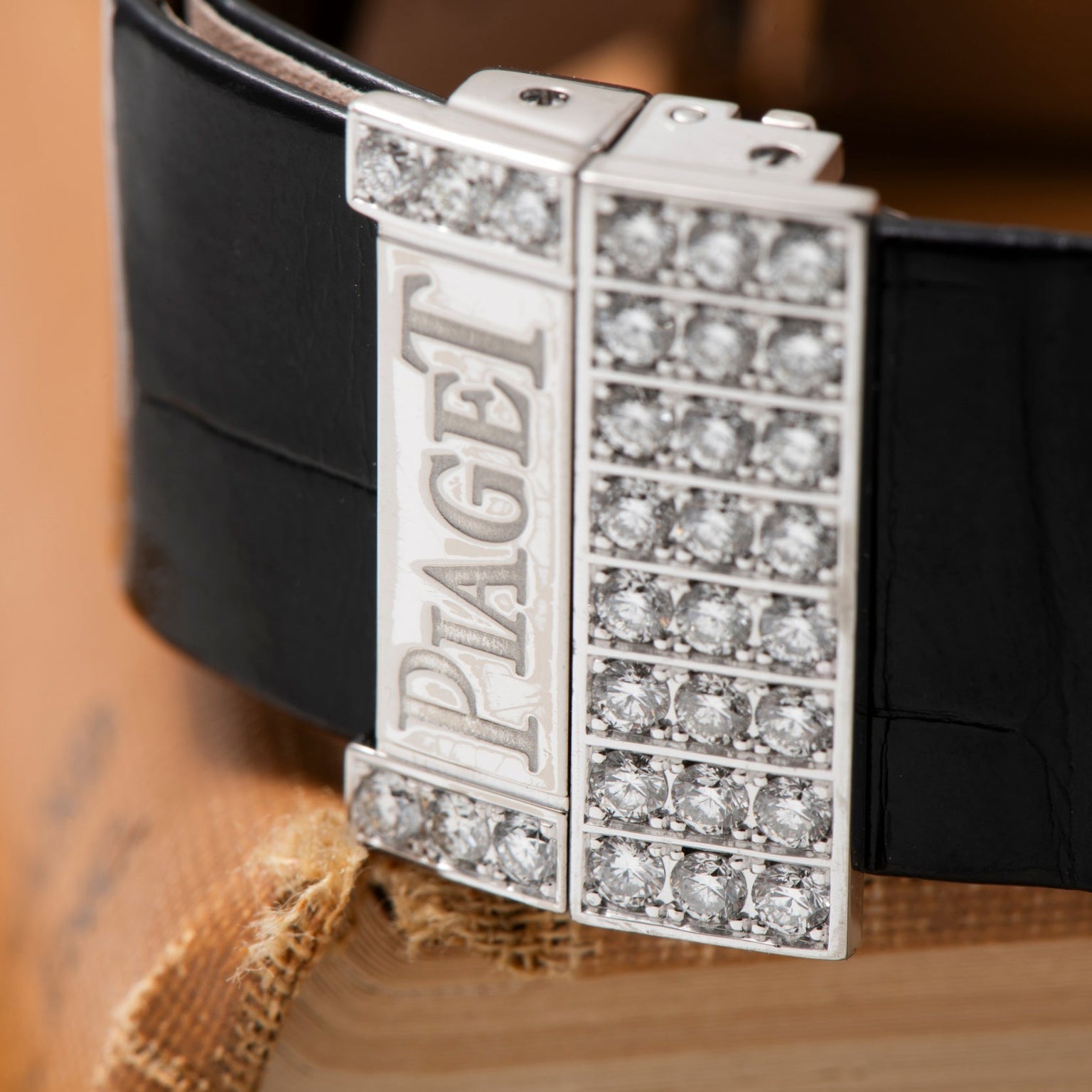 Close-up of the Piaget Limelight Baguette Diamond Dress Watch clasp, adorned with diamonds and set on a black leather strap, resting atop an old book.