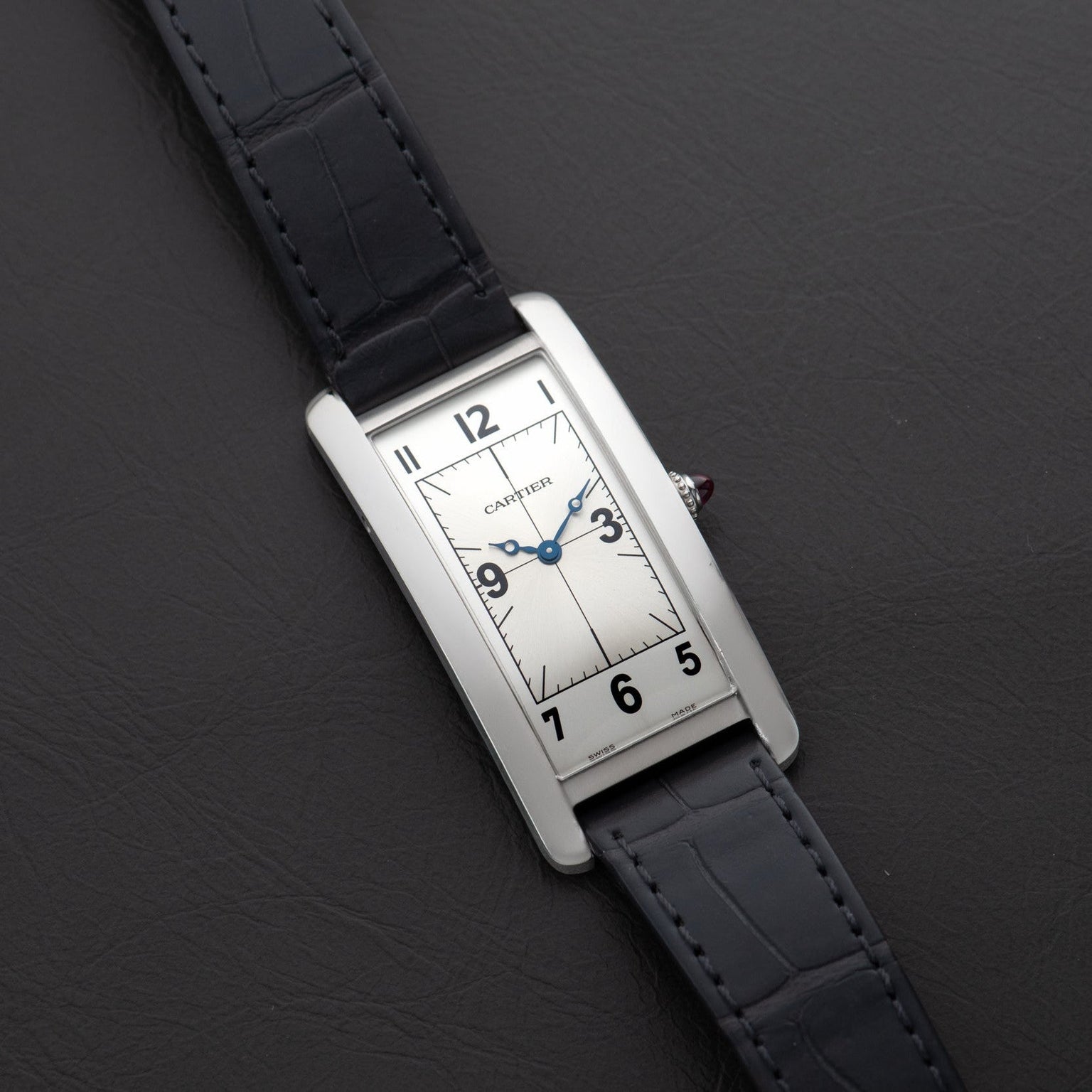 A Cartier Tank Cintrée Piece Unique rectangular wristwatch with a black leather strap rests on a dark leather surface.