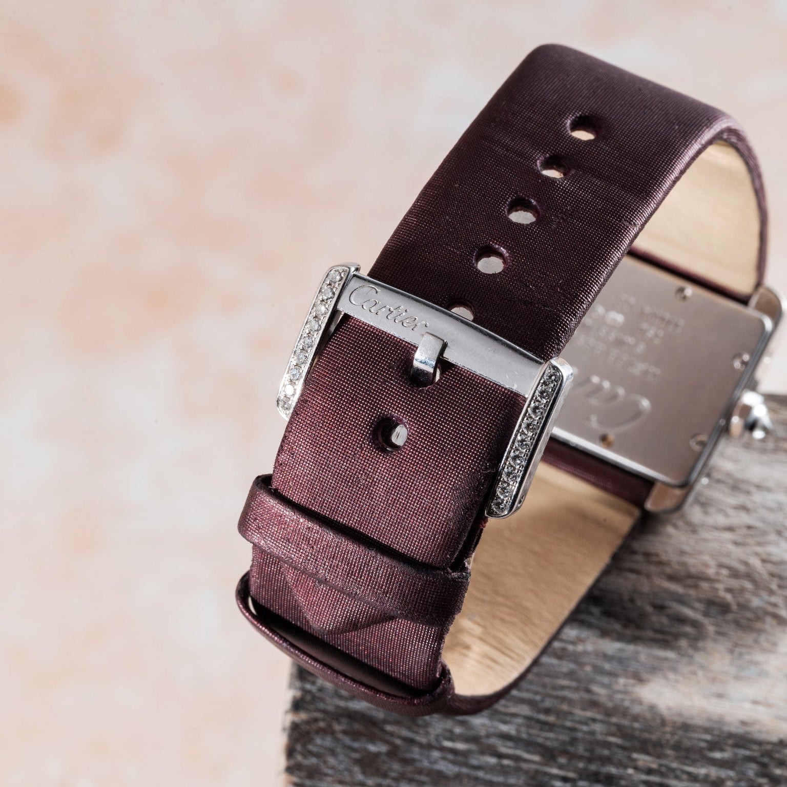 Close-up of a maroon Cartier Tank Divan watch strap with a silver buckle on a light textured background.