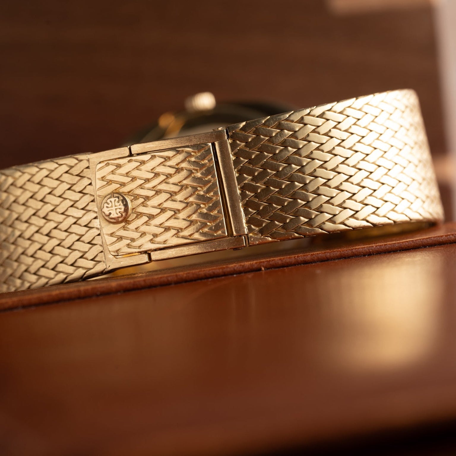 Close-up of the Patek Philippe Ellipse Jumbo gold woven watch band with clasp, resting on a brown leather surface.