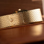 Close-up of the Patek Philippe Ellipse Jumbo gold woven watch band with clasp, resting on a brown leather surface.