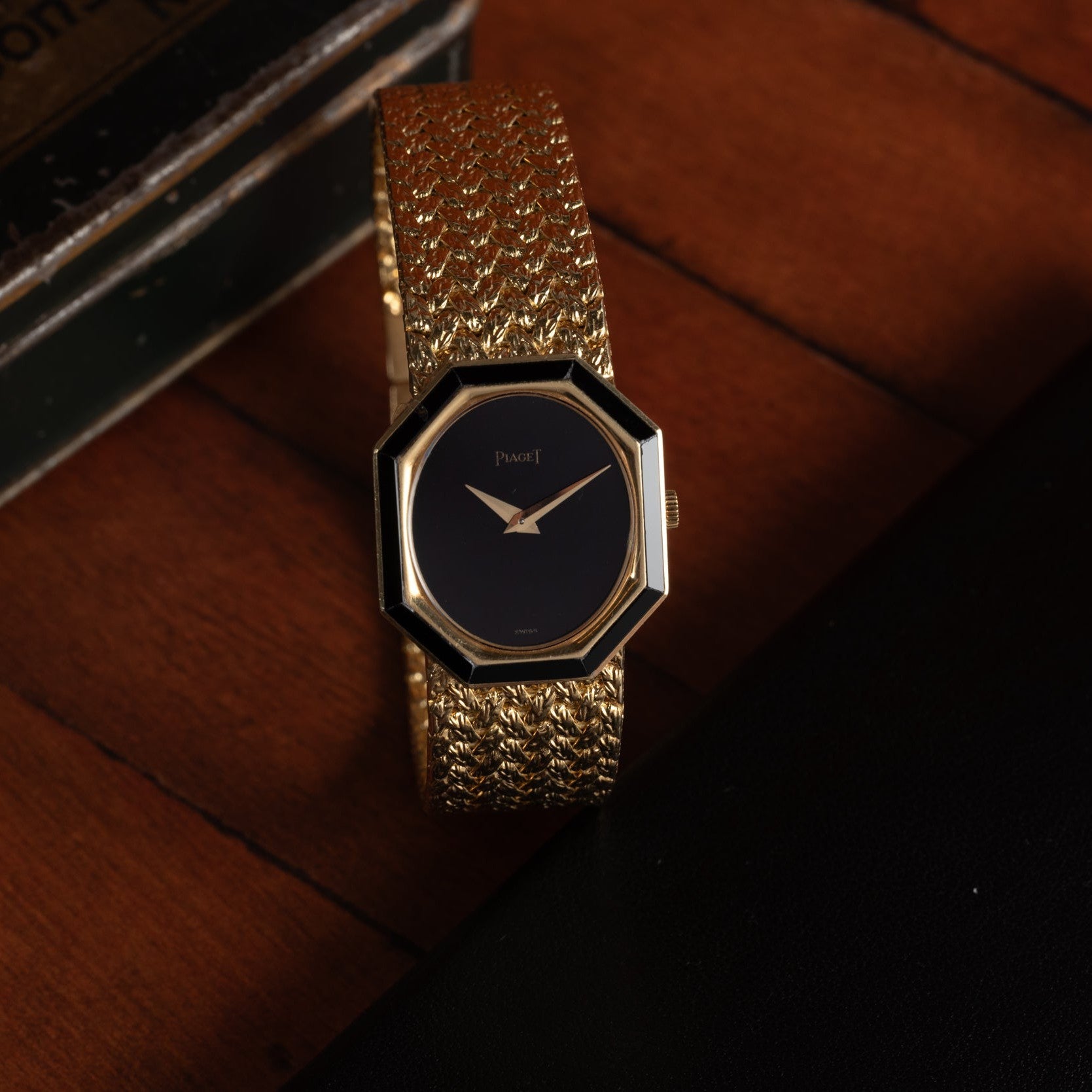 The Piaget Onyx Dial gold wristwatch with a black face rests on a wooden surface.