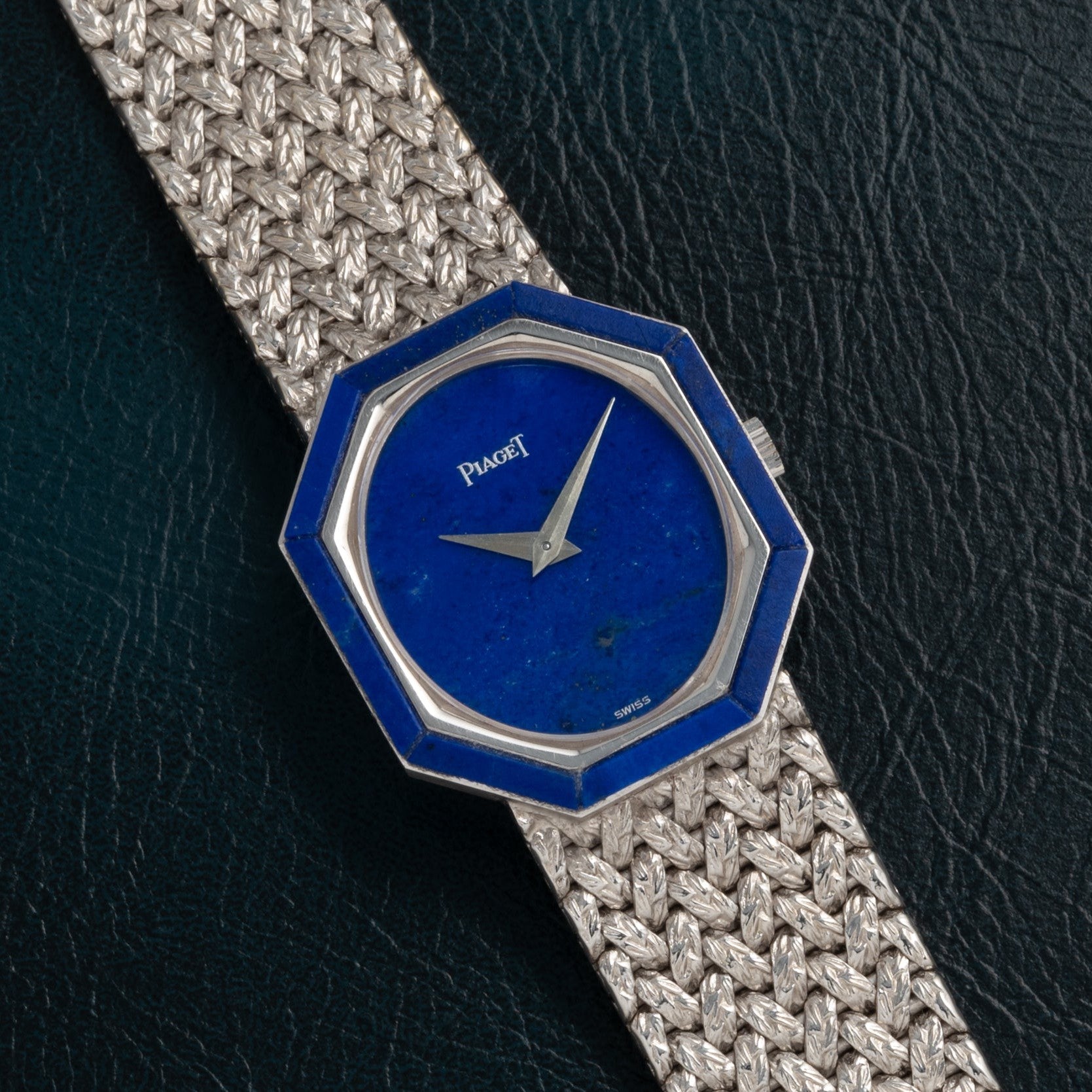 Piaget Lapis Lazuli White Gold Dress Watch with a hexagonal blue face and woven metal band displayed on a dark textured surface.