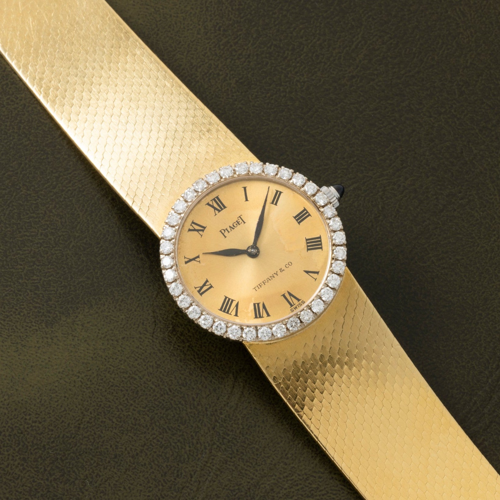 Piaget Ladies Diamond Watch for Tiffany & Co. with Roman numerals, diamond bezel, and textured gold band, displayed on a dark surface.