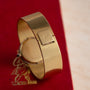 A Piaget Ladies Diamond Watch, Tiffany & Co., featuring a gold textured band and a P-engraved clasp, rests on a red surface.