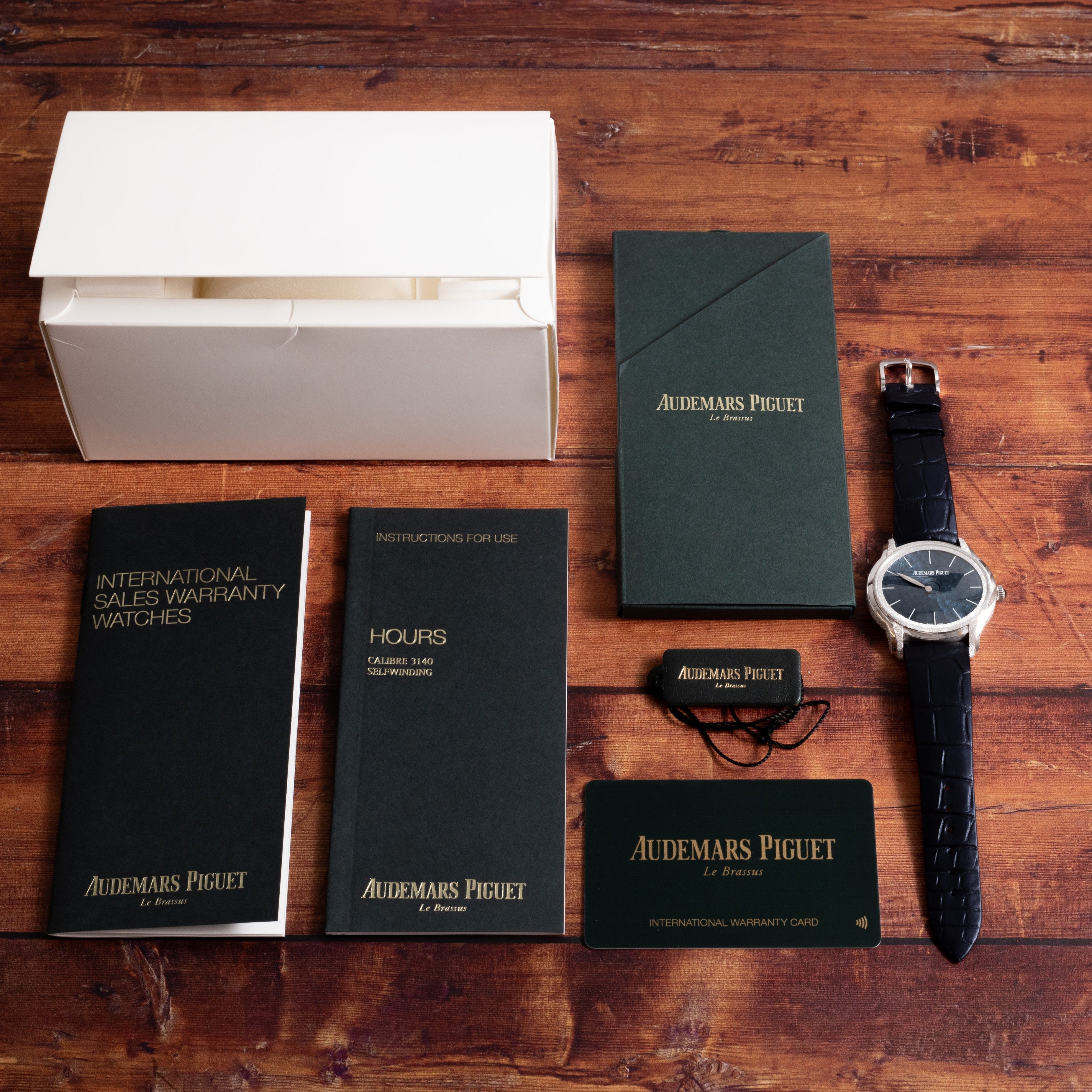 An Audemars Piguet Millenary Philosophique watch with warranty card, manuals, and box displayed on a wooden table.