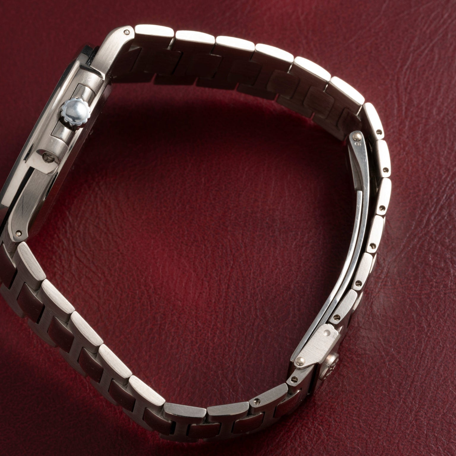 A Patek Philippe Nautilus silver wristwatch with a metal band rests on a textured red surface.