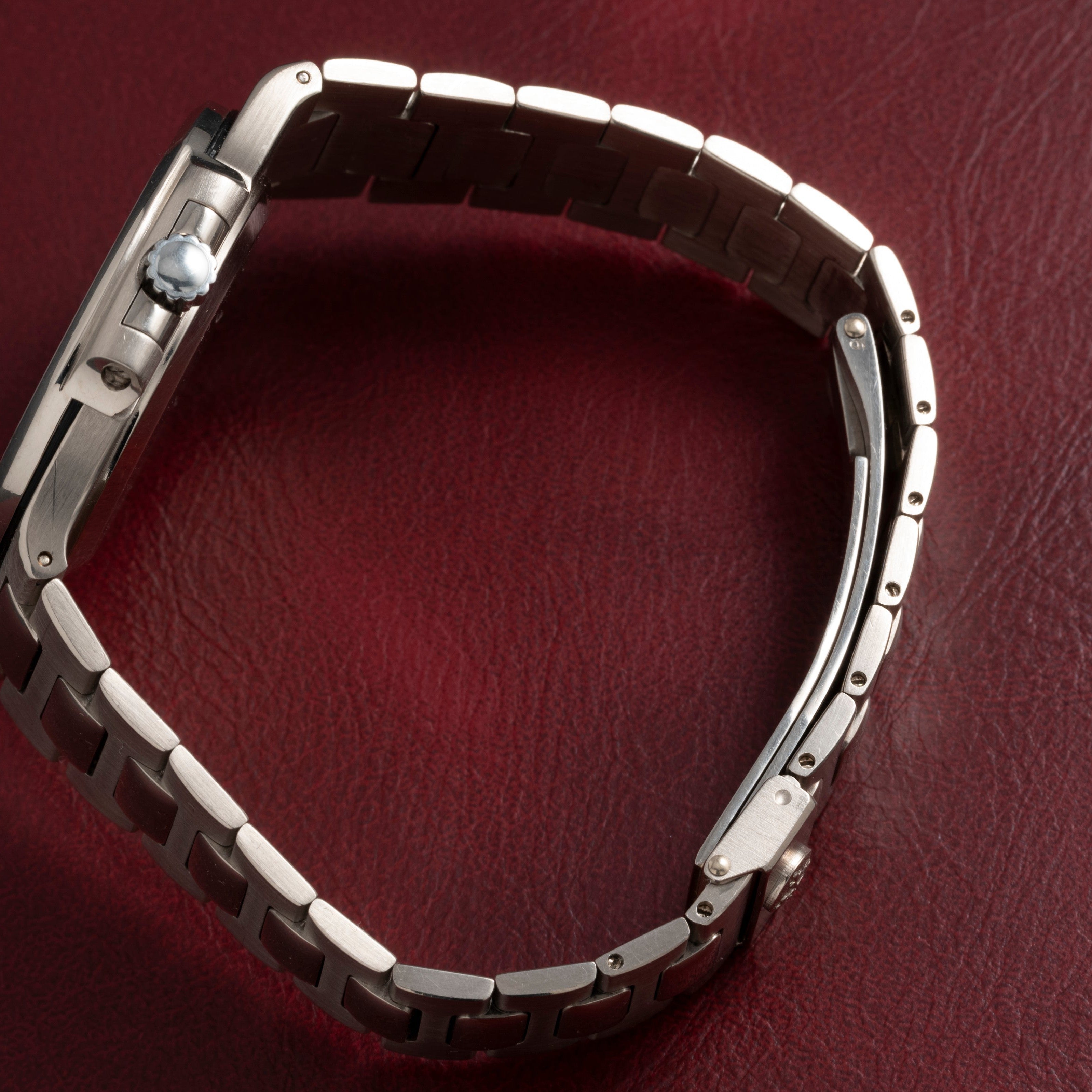 A Patek Philippe Nautilus silver wristwatch with a metal band rests on a textured red surface.