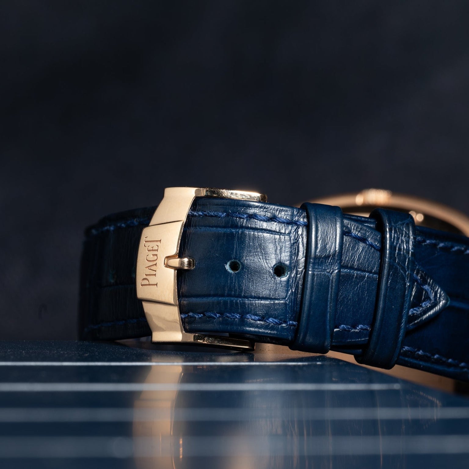 Close-up of the Piaget Black Tie Andy Warhol blue leather watch strap with a gold clasp, set against a dark background.