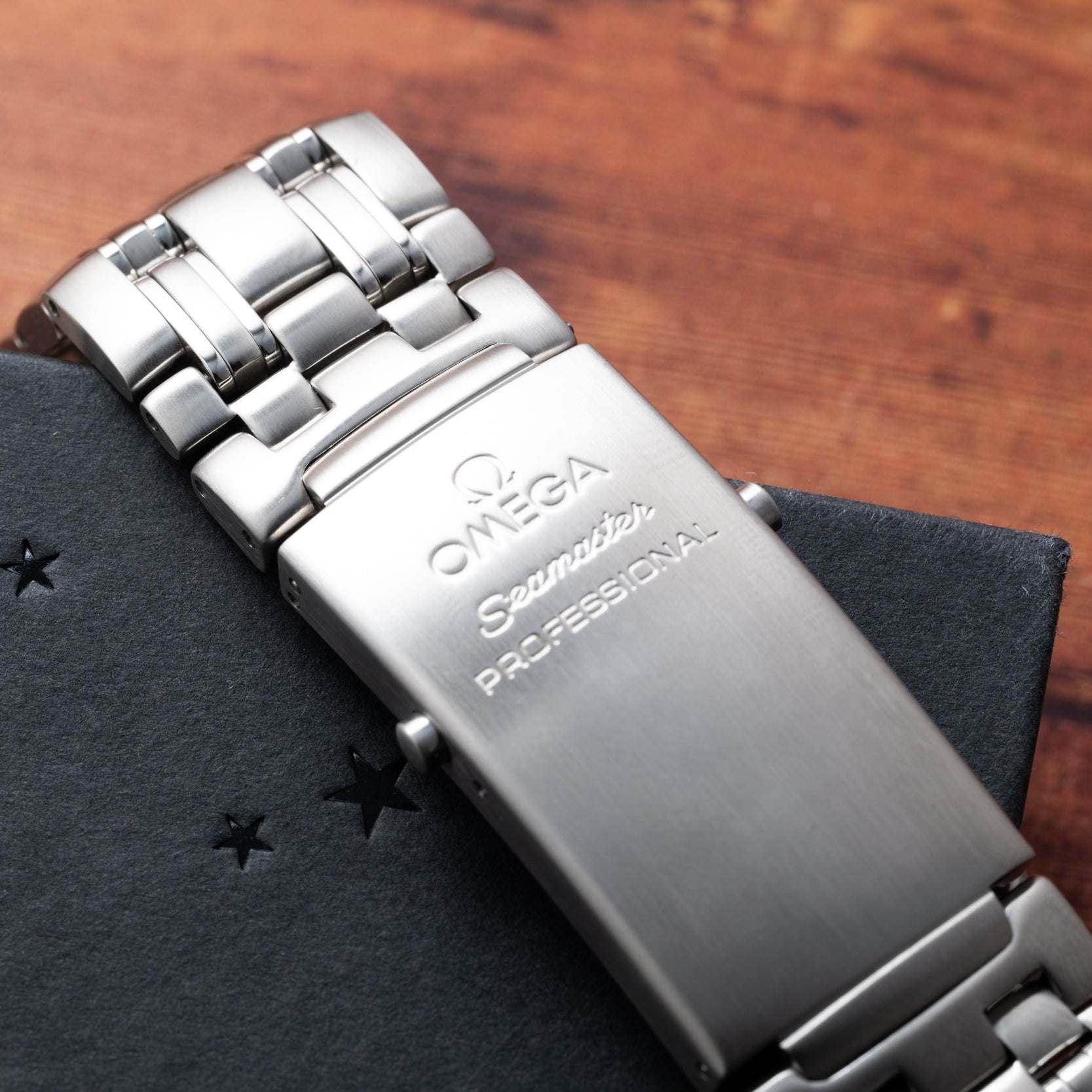 A close-up of an OMEGA Seamaster 300 Professional GMT stainless steel watch bracelet on a dark textured surface.