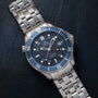 An OMEGA Seamaster 300 Professional GMT with a blue bezel and black dial rests on a dark leather surface.