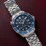 An OMEGA Seamaster 300 Professional GMT watch with a blue bezel rests on a maroon leather surface.