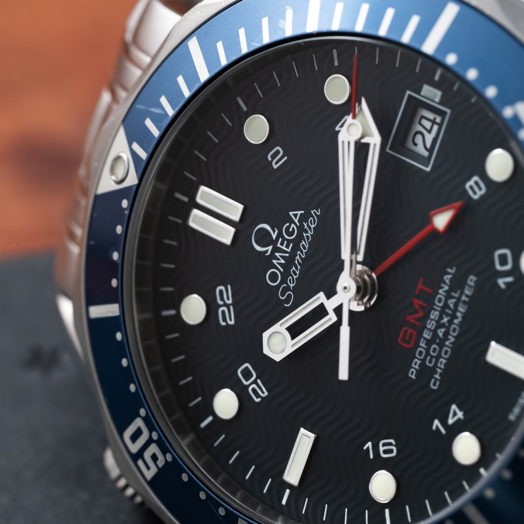 Close-up of an OMEGA Seamaster 300 Professional GMT watch featuring its face, hands, date window, and blue bezel.