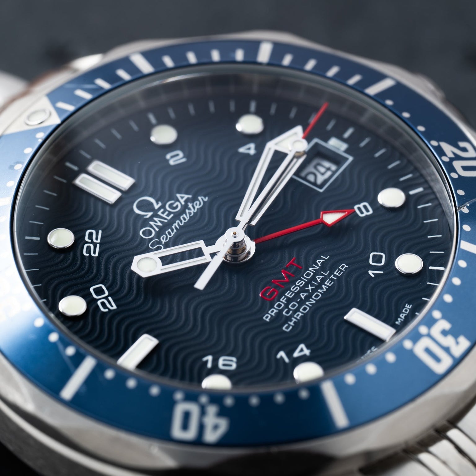 Close-up of the OMEGA Seamaster 300 Professional GMT watch face, featuring a blue bezel and red GMT hand.