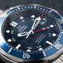 Close-up of the OMEGA Seamaster 300 Professional GMT watch face, featuring a blue bezel and red GMT hand.