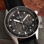 A close-up of a Blancpain Fifty Fathoms Bathyscaphe Chronographe Flyback wristwatch with a black strap displayed on a gray cushion.