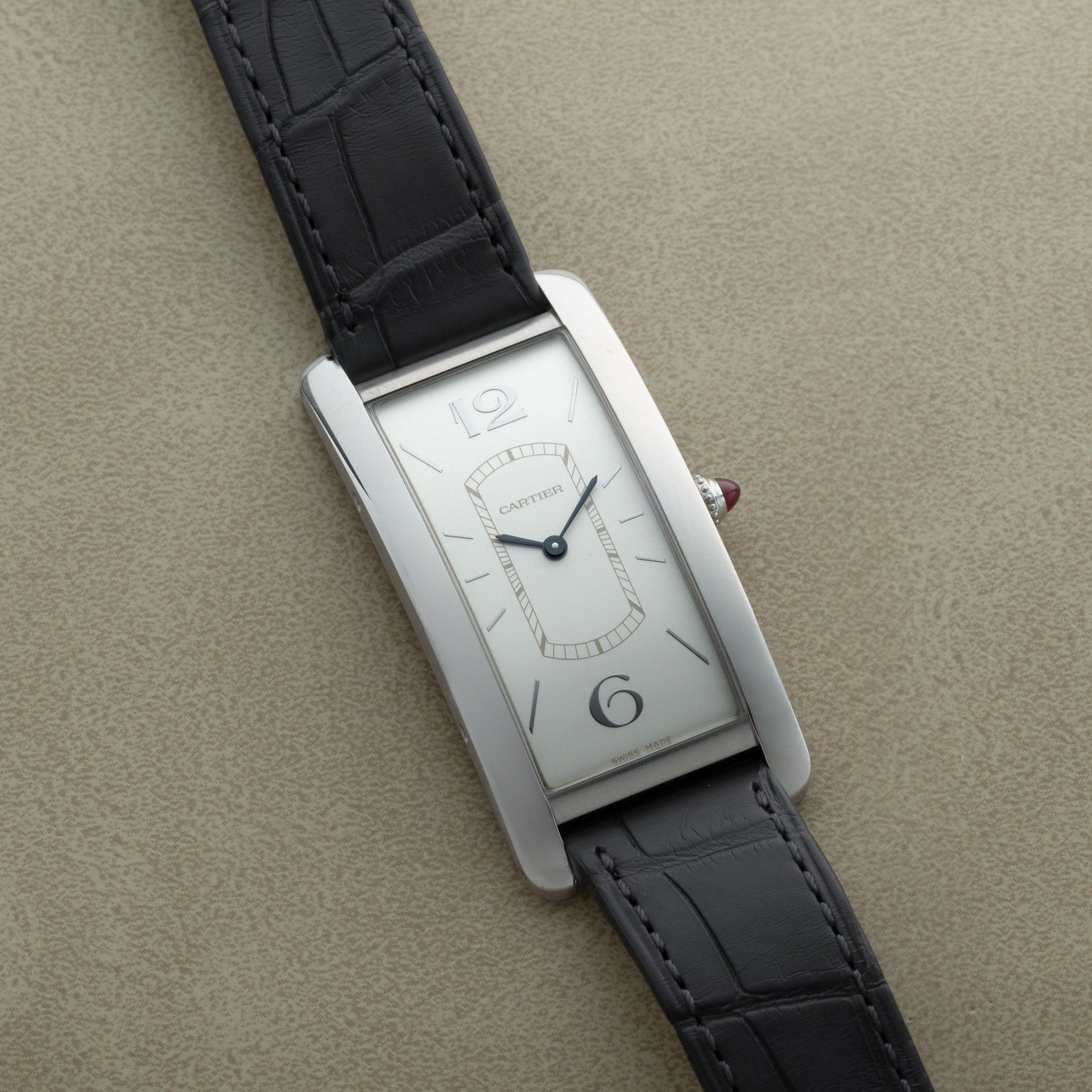 A Cartier Tank Cintrée Limited Edition rectangular wristwatch with a silver face and black leather strap displayed on a beige surface.