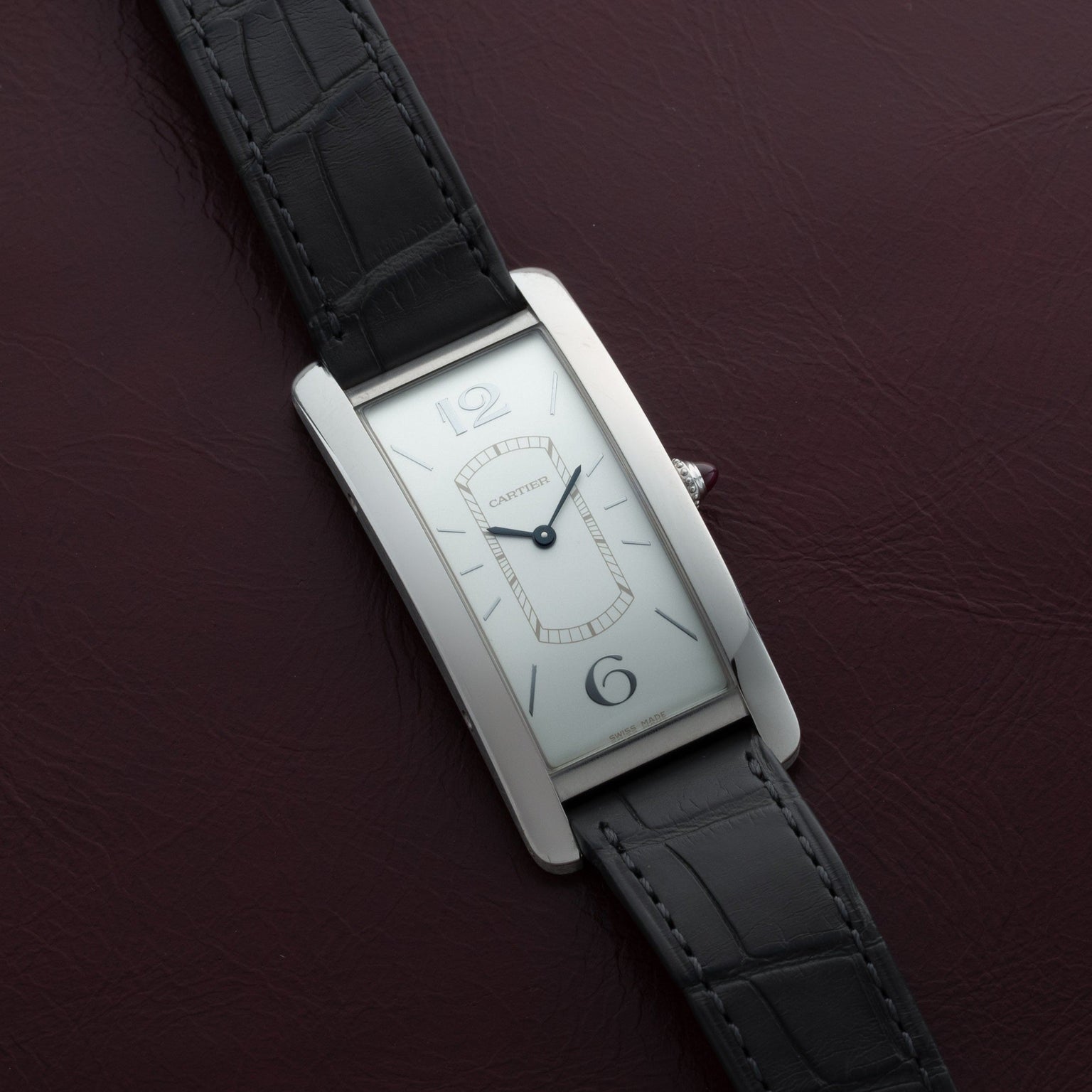 Cartier Tank Cintrée Limited Edition wristwatch with a black leather strap displayed on a dark maroon leather surface.