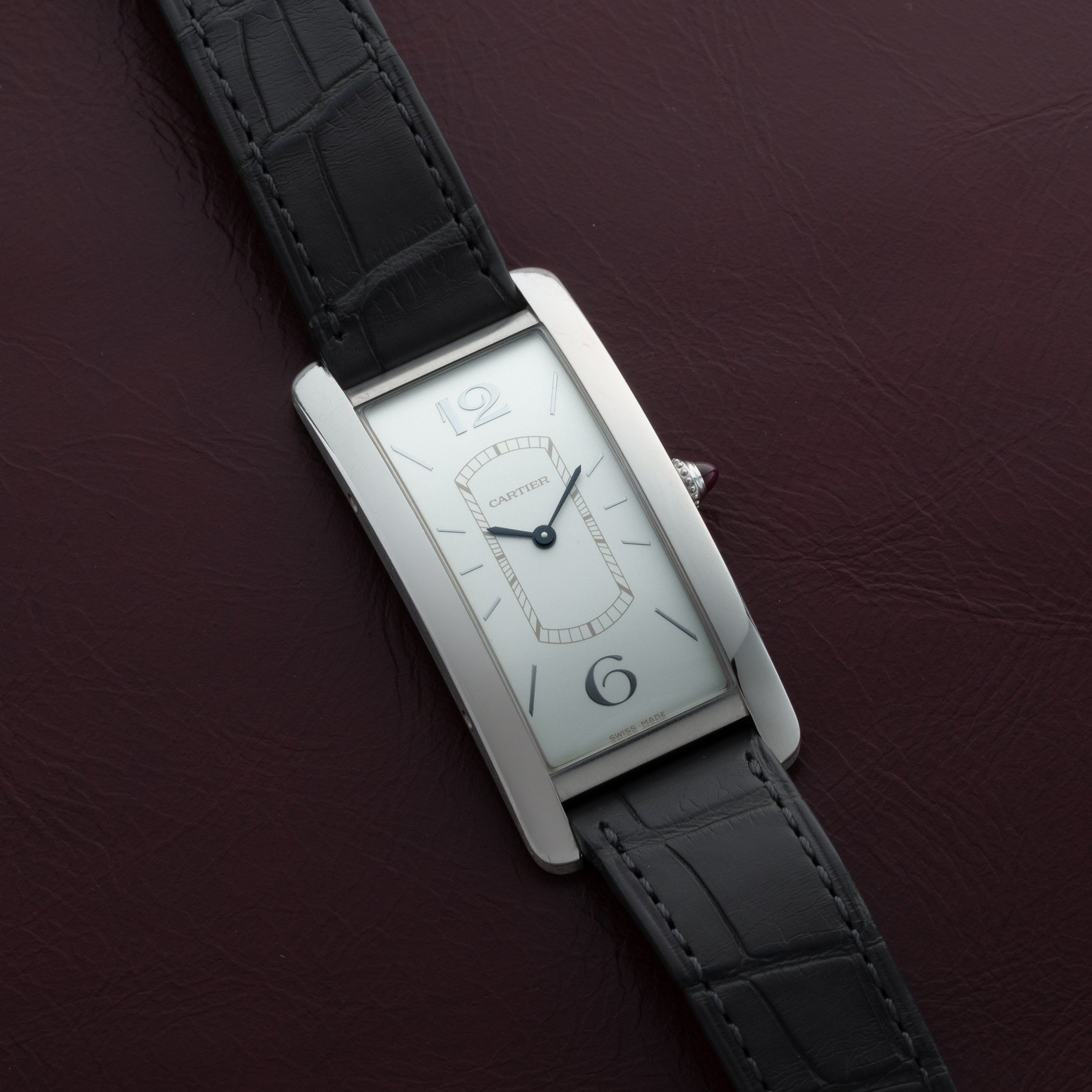 Cartier Tank Cintrée Limited Edition wristwatch with a black leather strap displayed on a dark maroon leather surface.