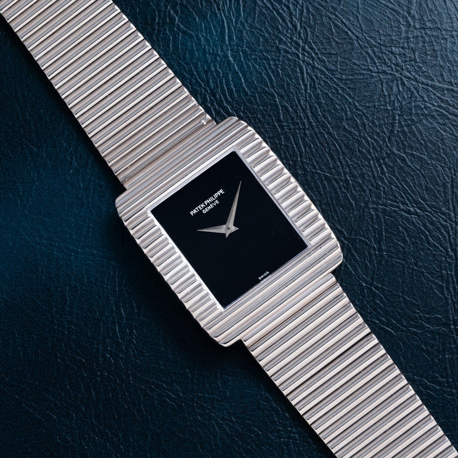 A Patek Philippe Ellipse Gondolo Onyx watch with a black square face is displayed on a dark textured surface.