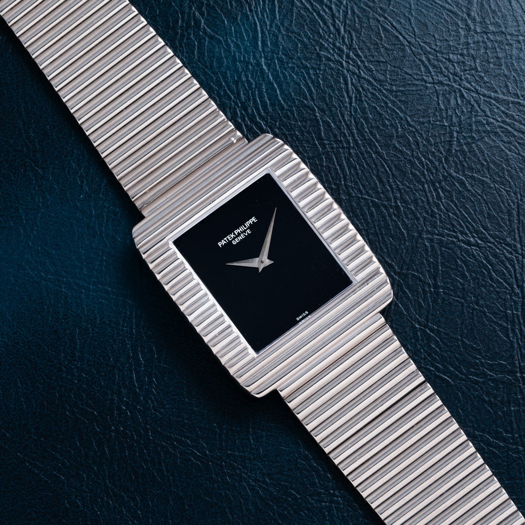 A Patek Philippe Ellipse Gondolo Onyx watch with a black square face is displayed on a dark textured surface.