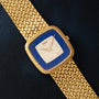 Piaget Pave Lapis Lazuli Dress Watch with a diamond-studded blue square face and textured gold band, displayed on a dark surface.