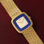 Piaget Pave Lapis Lazuli Dress Watch with a diamond-set face and blue border, displayed on a textured burgundy surface.