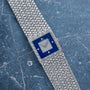 The Piaget Tradition Lapis Lazuli Diamond Dress Watch features a blue square face and textured silver band, exuding luxury on a marble surface.