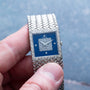 A hand holding a Piaget Tradition Lapis Lazuli Diamond Dress Watch with a blue face and diamond-studded square center.
