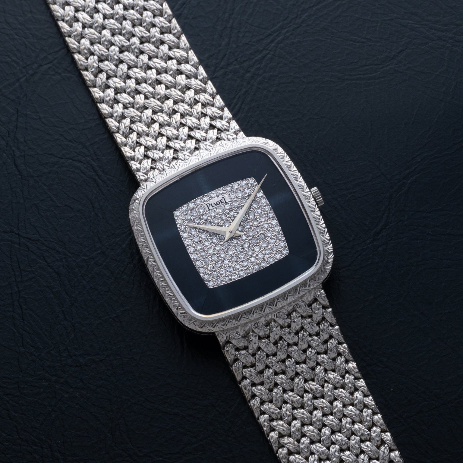 The Piaget Hawk Eye White Gold Dress Watch features a diamond-studded square face and textured metal band, elegantly displayed on a black surface.