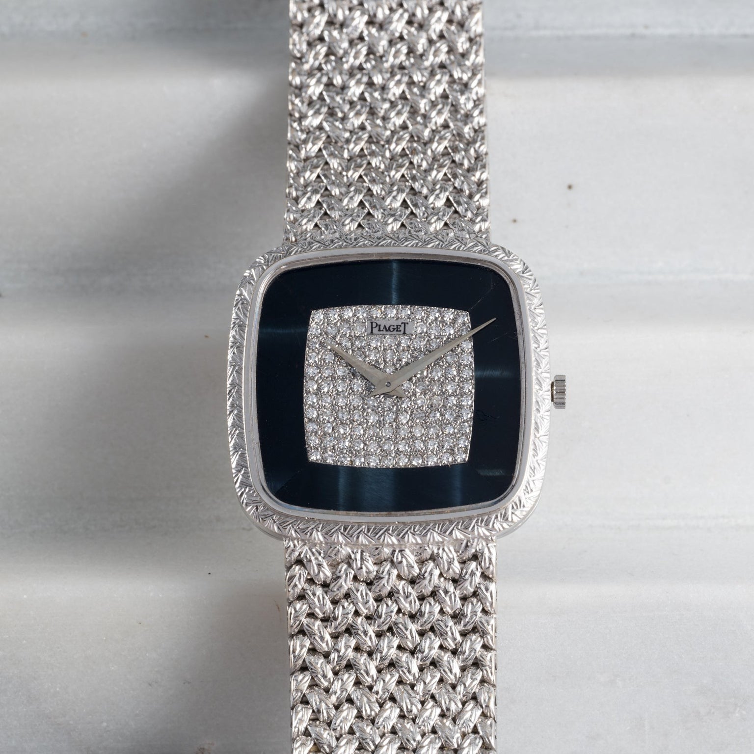 The Piaget Hawk Eye White Gold Dress Watch features a textured band and a diamond-studded square face, displayed on a light surface.