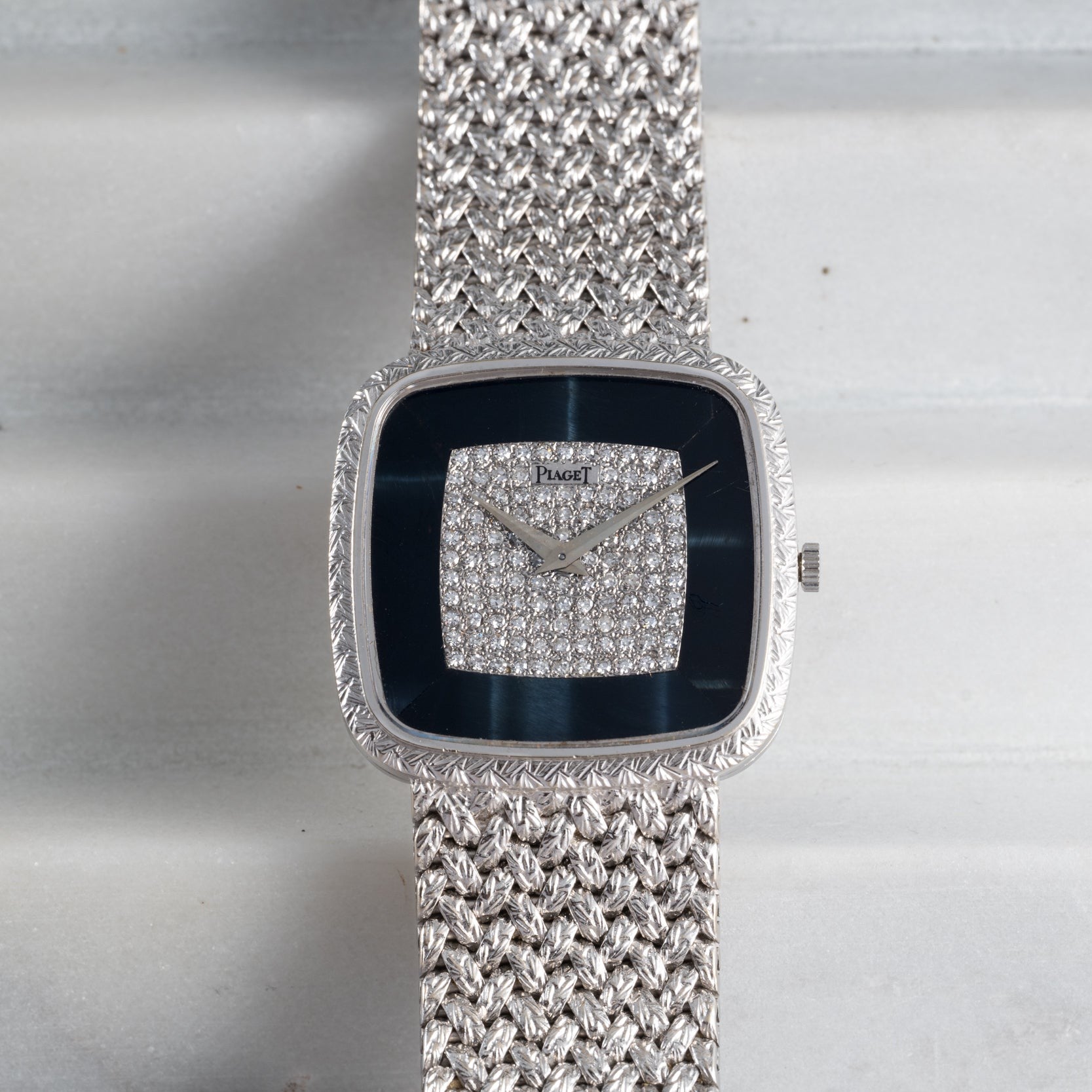 The Piaget Hawk Eye White Gold Dress Watch features a textured band and a diamond-studded square face, displayed on a light surface.