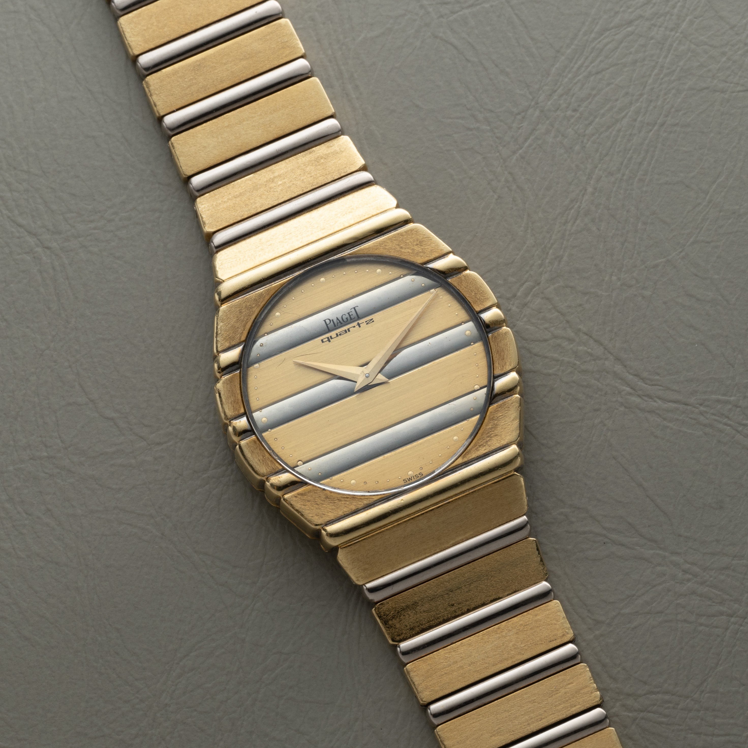 Piaget Polo Two-Tone quartz wristwatch with gold and silver stripes displayed on a textured gray surface.