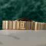 Close-up of the Piaget Polo Two-Tone watch band, featuring a P engraved on the clasp, set against a green background.