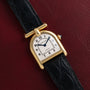 Cartier Calandre gold wristwatch with a black leather band displayed on a dark red textured surface.