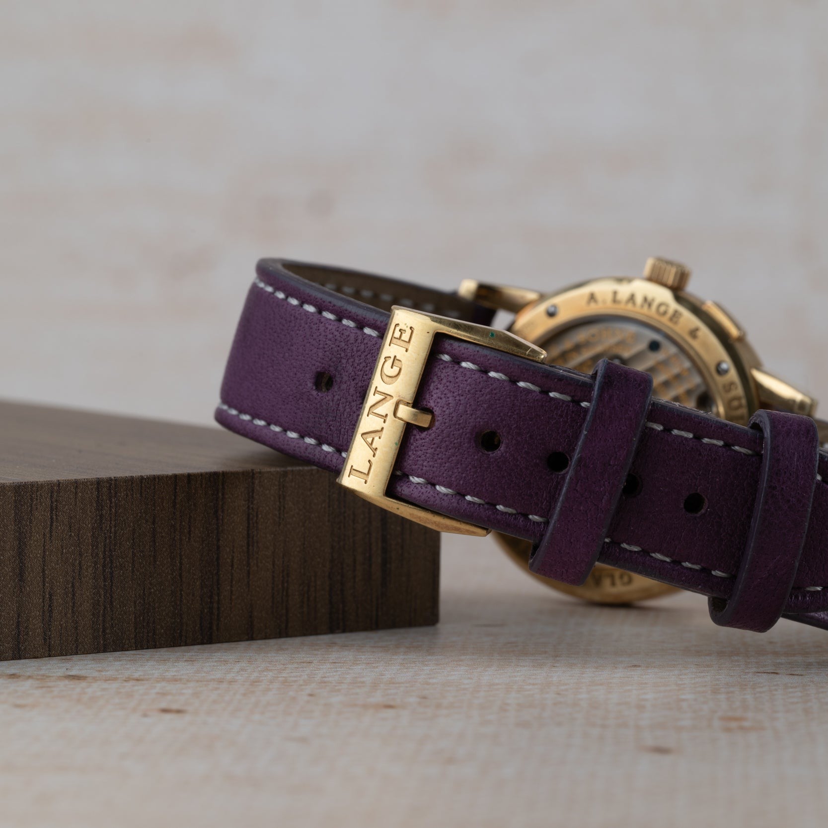 Close-up of a purple leather watch strap from the Saxonia Outsize Date by Lange & Sohne, featuring LANGE engraved on its gold buckle.