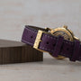 Close-up of a purple leather watch strap from the Saxonia Outsize Date by Lange & Sohne, featuring LANGE engraved on its gold buckle.